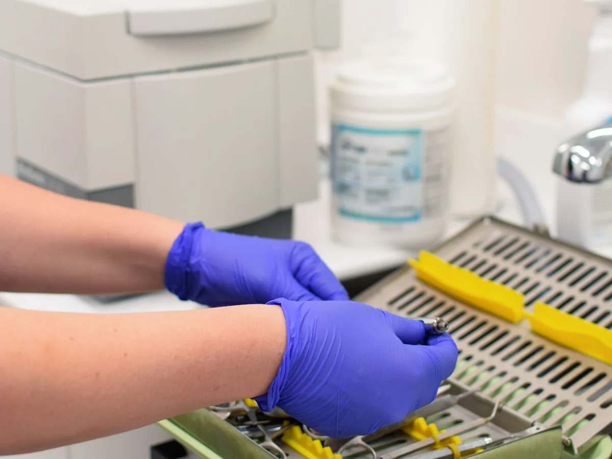 Gloved team member preparing dental instruments in the sterilization area